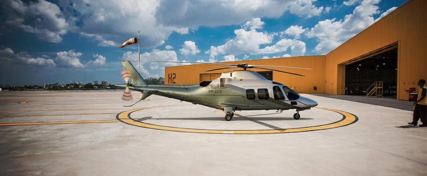 Helicóptero biturbina prata e verde-oliva no heliponto, diante de um hangar